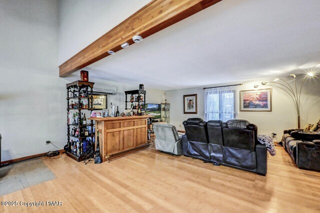 living room featuring light wood-type flooring, beamed ceiling, and indoor bar