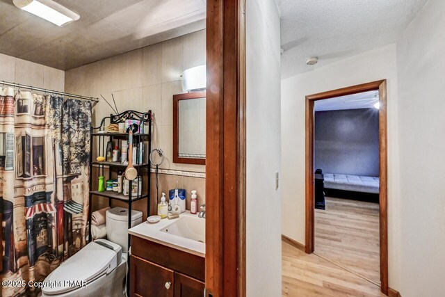 bathroom with vanity, wood-type flooring, a textured ceiling, a shower with curtain, and toilet