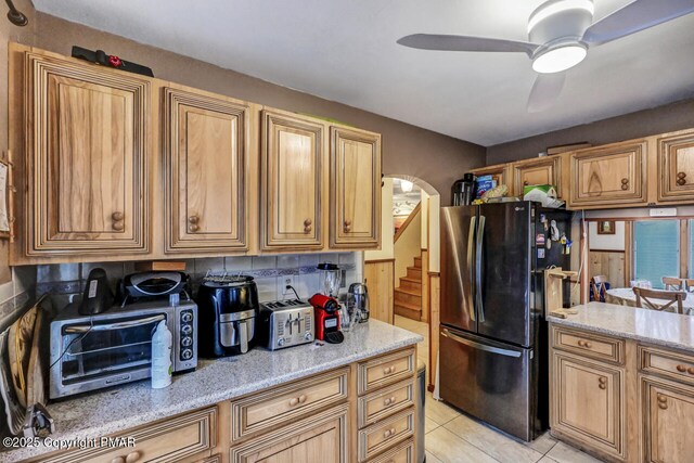 kitchen featuring light tile patterned floors, stainless steel refrigerator, ceiling fan, backsplash, and light stone counters