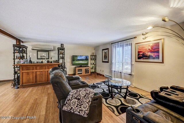 living room with baseboard heating, light hardwood / wood-style floors, a wall unit AC, and a textured ceiling