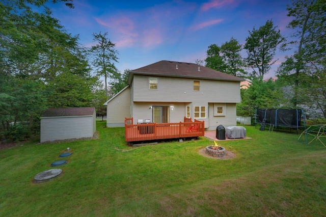 5117 Hounds Ear Rd, Tobyhanna, PA 18466 - back of house at dusk featuring a trampoline, a fire pit, a wooden deck, a shed, and a lawn