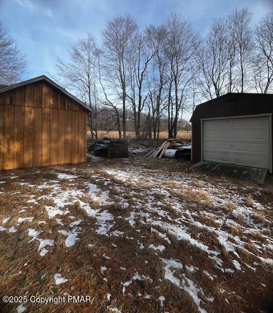 yard layered in snow featuring an outbuilding and a garage