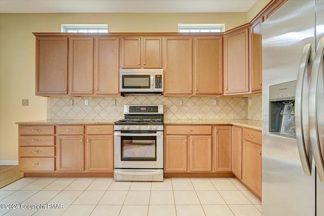 kitchen with appliances with stainless steel finishes, light tile patterned floors, backsplash, and light stone counters