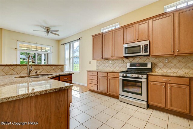 kitchen with light tile patterned flooring, sink, appliances with stainless steel finishes, ceiling fan, and light stone countertops