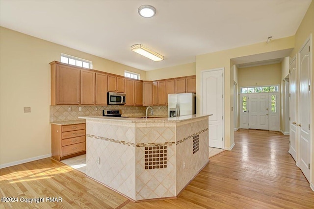 kitchen with backsplash, light hardwood / wood-style flooring, an island with sink, and appliances with stainless steel finishes