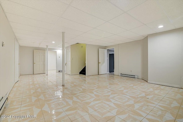 basement with a baseboard radiator, light tile patterned floors, and a drop ceiling