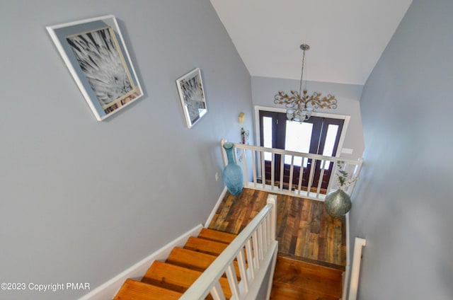 stairway featuring an inviting chandelier, baseboards, vaulted ceiling, and wood finished floors