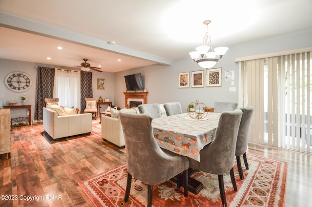 dining space with beam ceiling, a fireplace, recessed lighting, wood finished floors, and ceiling fan with notable chandelier