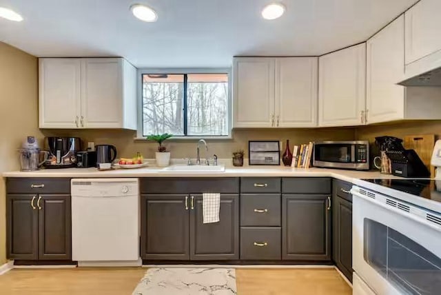 kitchen with a sink, gray cabinetry, white cabinets, light wood-style floors, and white appliances