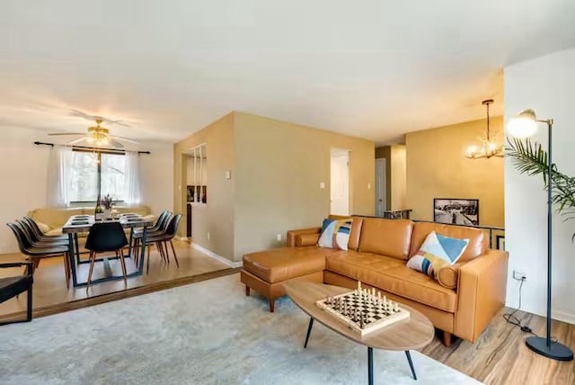 living area featuring baseboards, wood finished floors, and ceiling fan with notable chandelier