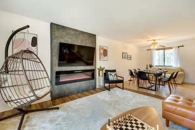living area with a glass covered fireplace, a ceiling fan, and wood finished floors