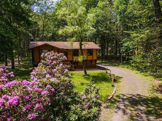exterior space featuring a view of trees, driveway, a chimney, and a front lawn