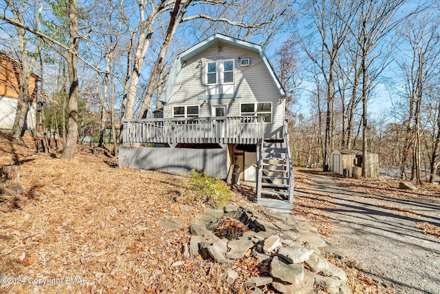 view of front of property featuring a wooden deck, a gambrel roof, stairway, an outdoor structure, and a shed