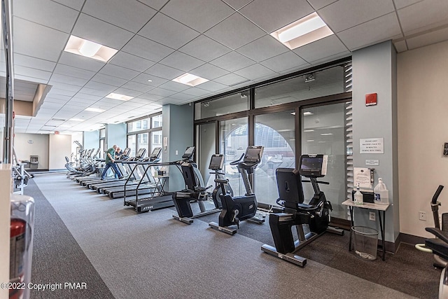 workout area with baseboards, a wall of windows, and a drop ceiling