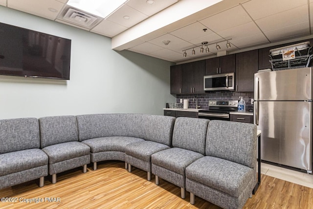 living area with a drop ceiling, light wood-type flooring, and visible vents