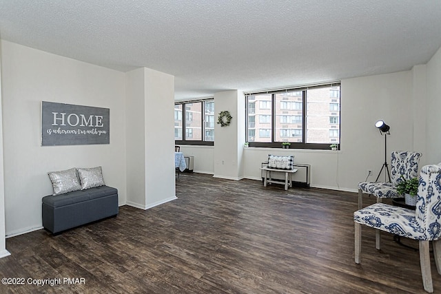 living area featuring a textured ceiling, baseboards, and wood finished floors