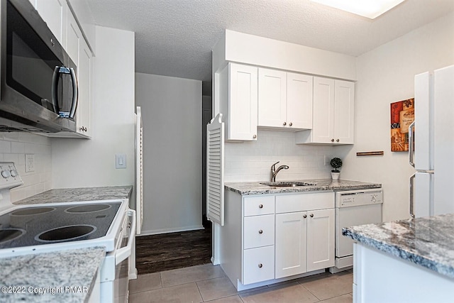 kitchen featuring white appliances, light tile patterned flooring, a sink, and white cabinets