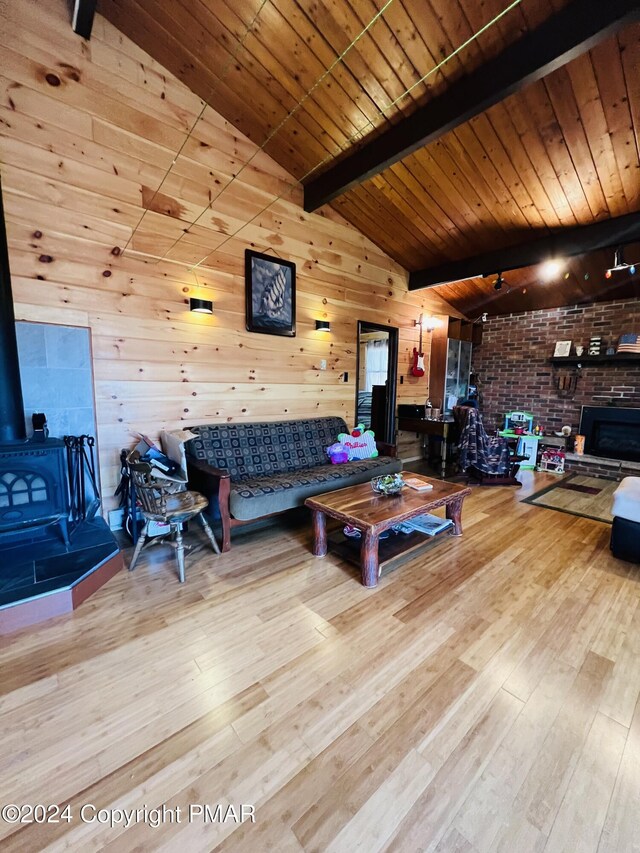 living area with wood finished floors, lofted ceiling with beams, a wood stove, wood walls, and wooden ceiling