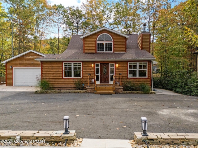 cabin with driveway, a shingled roof, a chimney, and faux log siding