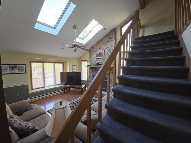 living area with a skylight, stairway, baseboard heating, a ceiling fan, and wood finished floors