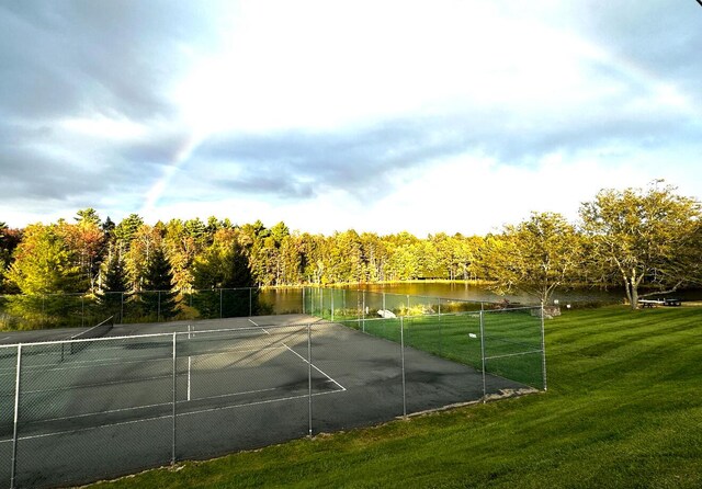 view of sport court with a water view, fence, and a yard