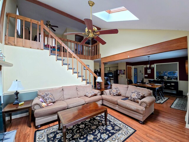 living area featuring high vaulted ceiling, ceiling fan with notable chandelier, wood finished floors, baseboards, and stairs