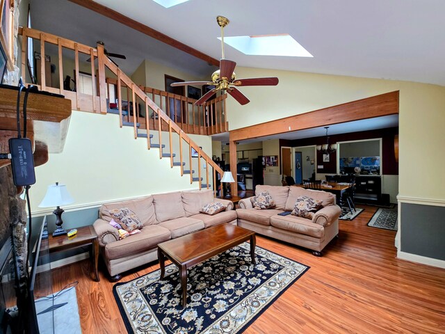 living area featuring lofted ceiling with skylight, ceiling fan, stairway, and wood finished floors