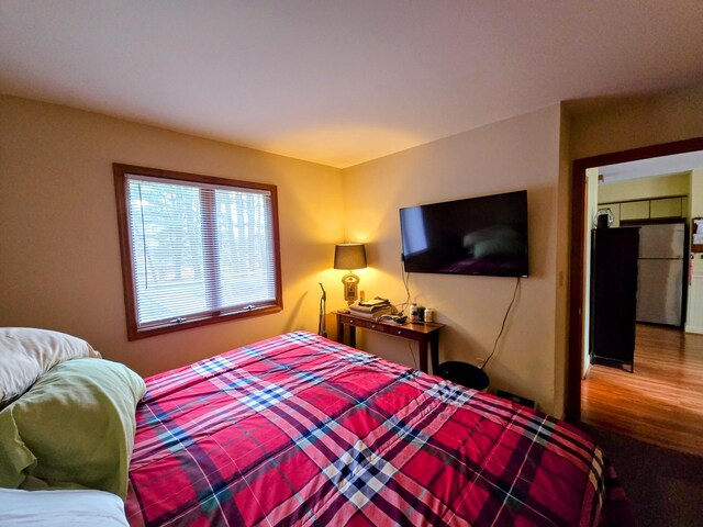 bedroom featuring wood finished floors and freestanding refrigerator