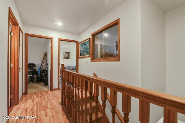 corridor with light wood-style floors and an upstairs landing