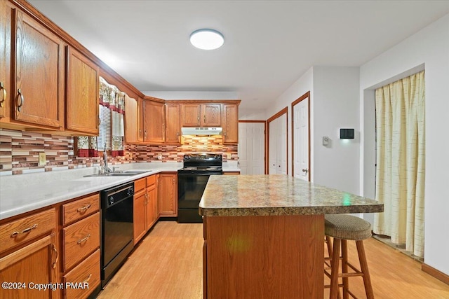 kitchen with black appliances, light wood-style floors, a sink, and under cabinet range hood