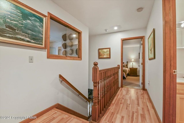 corridor with baseboards, light wood-style flooring, and an upstairs landing