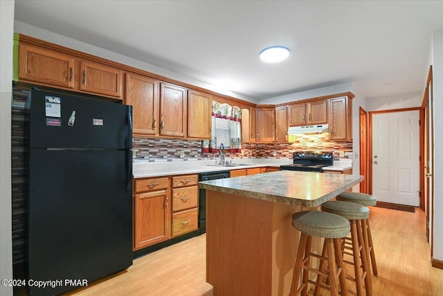 kitchen with light wood-style floors, brown cabinets, under cabinet range hood, and black appliances