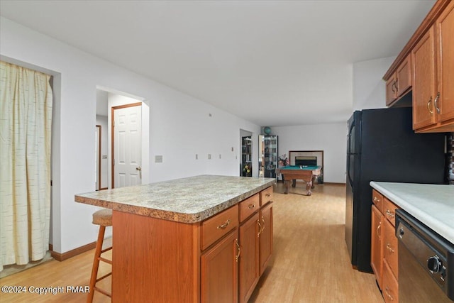 kitchen with light wood finished floors, brown cabinetry, a center island, light countertops, and black appliances