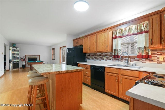 kitchen with tasteful backsplash, a kitchen island, a sink, light wood-type flooring, and black appliances