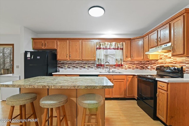 kitchen featuring light countertops, a sink, black appliances, under cabinet range hood, and a kitchen breakfast bar