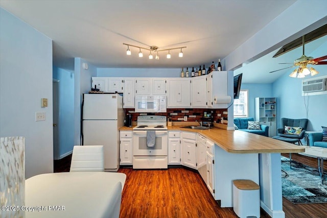 kitchen with a kitchen bar, dark hardwood / wood-style floors, kitchen peninsula, white appliances, and white cabinets