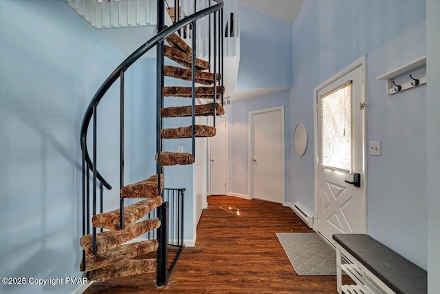 entryway with dark wood-type flooring, a baseboard radiator, and a towering ceiling