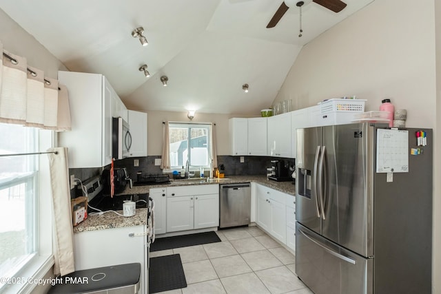 kitchen with stainless steel appliances, white cabinetry, lofted ceiling, and dark stone countertops