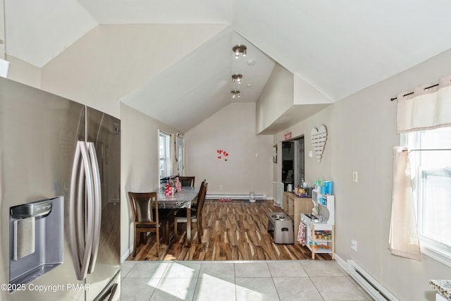 kitchen with a baseboard radiator, lofted ceiling, light tile patterned floors, and stainless steel fridge