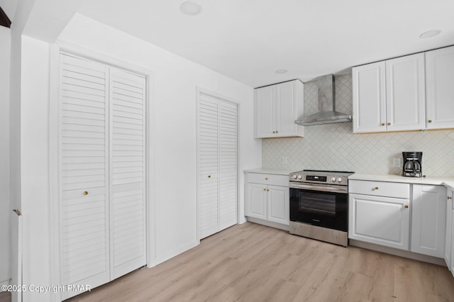 kitchen featuring wall chimney range hood, stainless steel electric range oven, white cabinetry, and light wood-style floors