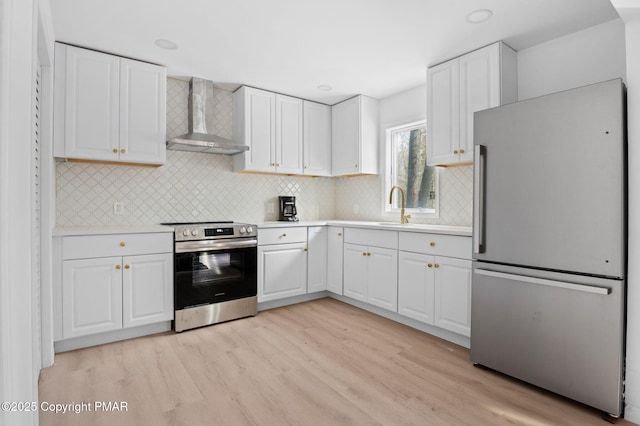 kitchen with stainless steel appliances, light countertops, light wood-style floors, white cabinetry, and wall chimney exhaust hood