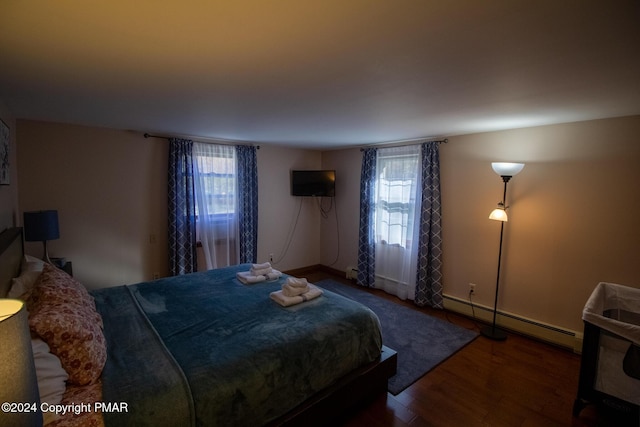 bedroom featuring multiple windows, a baseboard heating unit, and wood finished floors