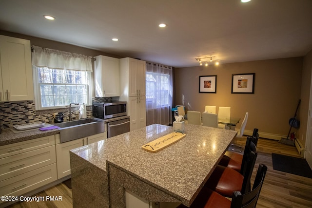 kitchen with dark wood-style floors, stainless steel appliances, backsplash, a kitchen island, and a sink