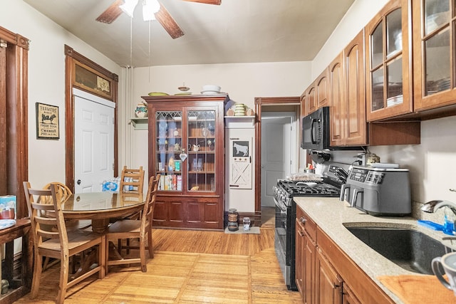 kitchen featuring glass insert cabinets, ceiling fan, black microwave, stainless steel gas range, and a sink