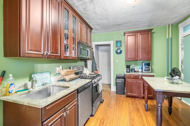 kitchen featuring light wood-style flooring, a sink, stainless steel appliances, glass insert cabinets, and a textured ceiling