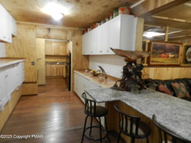 kitchen featuring wooden walls, white cabinetry, a breakfast bar area, light stone counters, and dark wood-type flooring