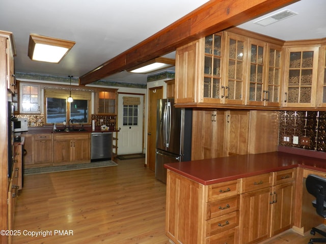 kitchen with stainless steel appliances, dark countertops, light wood-style flooring, a sink, and a peninsula