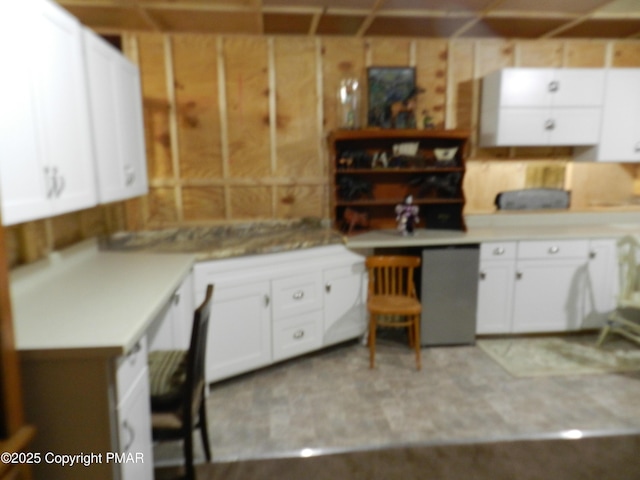 kitchen with wooden walls, white cabinetry, and light countertops