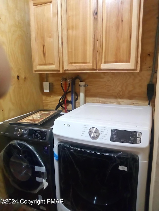 laundry area featuring washing machine and clothes dryer, cabinet space, and wooden walls