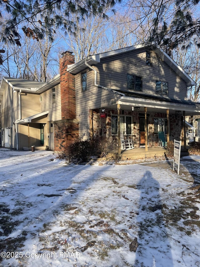 view of snow covered exterior featuring a chimney and a porch